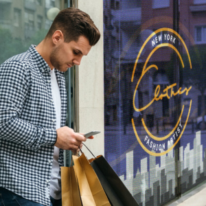 Man checking phone holding shopping bags standing in front of window graphics